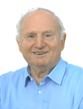 Älterer Mann mit kurzem, grauem Haar und einem freundlichen Lächeln, trägt ein blaues Hemd.