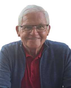 L&auml;chelnder &auml;lterer Mann mit Brille, rotem Polohemd und blauer Strickjacke vor einem wei&szlig;en Hintergrund.