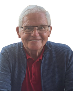 L&auml;chelnder &auml;lterer Mann mit Brille, rotem Polohemd und blauer Strickjacke vor einem wei&szlig;en Hintergrund.