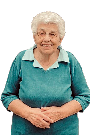 L&auml;chelnde &auml;ltere Frau mit blonden Locken, in blauem Pullover, steht mit verschr&auml;nkten H&auml;nden vor neutralem Hintergrund.