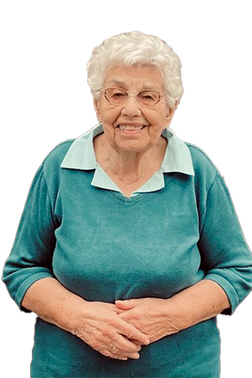 L&auml;chelnde &auml;ltere Frau mit blonden Locken, in blauem Pullover, steht mit verschr&auml;nkten H&auml;nden vor neutralem Hintergrund.