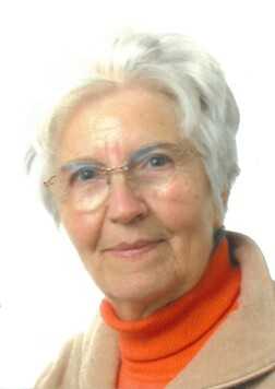 Portrait einer &auml;lteren Frau mit grauen Haaren, Brille und orangefarbenem Pullover vor wei&szlig;em Hintergrund.