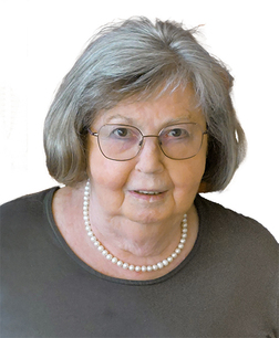 &Auml;ltere Frau mit Brille und grauen Haaren, tr&auml;gt eine Perlenkette und ein dunkles Oberteil, l&auml;chelt in die Kamera.