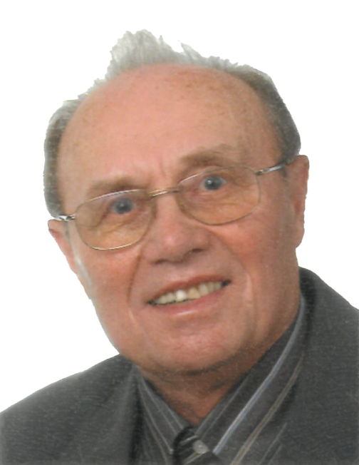 Portr&auml;t eines &auml;lteren Mannes mit Brille und grauen Haaren, l&auml;chelnd vor einem wei&szlig;en Hintergrund.