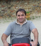 Mann sitzt auf einem roten Fahrzeug vor einer steinernen Wand in einer ländlichen Umgebung.