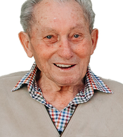 L&auml;chelnder &auml;lterer Mann mit grauen Haaren tr&auml;gt ein kariertes Hemd und eine beigefarbene Jacke.