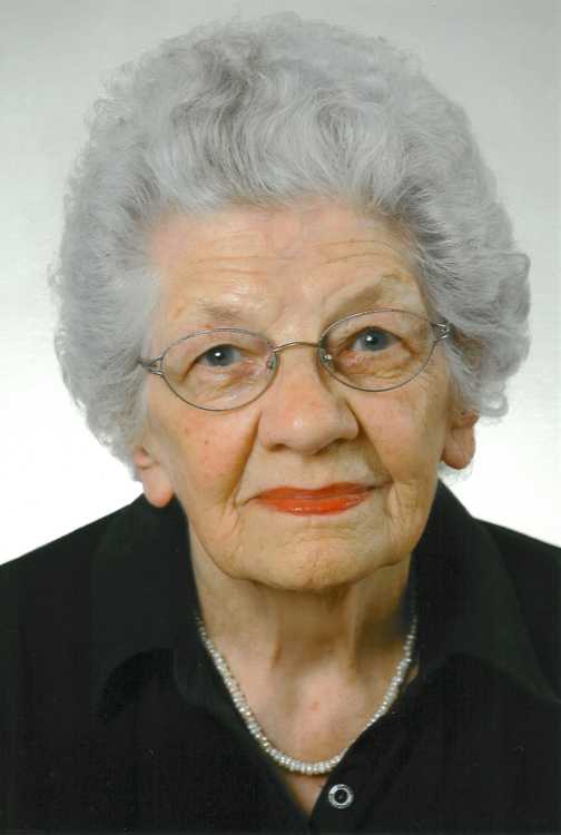 Portr&auml;t einer &auml;lteren Frau mit grauen Locken, Brille und rotem Lippenstift, bekleidet mit einem schwarzen Oberteil.