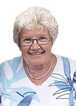 L&auml;chelnde &auml;ltere Frau mit blonden, lockigen Haaren, Brille und einer Bluse mit floralem Muster.