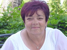 Porträt einer Frau mit kurzen, rotbraunen Haaren, lächelnd vor grünen Blättern im Hintergrund. Sie trägt ein weißes Oberteil.