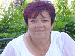 Portr&auml;t einer Frau mit kurzen, rotbraunen Haaren, l&auml;chelnd vor gr&uuml;nen Bl&auml;ttern im Hintergrund. Sie tr&auml;gt ein wei&szlig;es Oberteil.