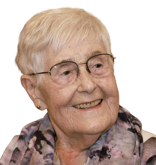 L&auml;chelnde &auml;ltere Frau mit kurz geschnittenem, grauem Haar und Brille, tr&auml;gt ein buntes Tuch um den Hals.