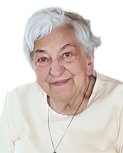 Portr&auml;t einer &auml;lteren Frau mit grauen Haaren, die in einem hellen Oberteil l&auml;chelt, vor neutralem Hintergrund.