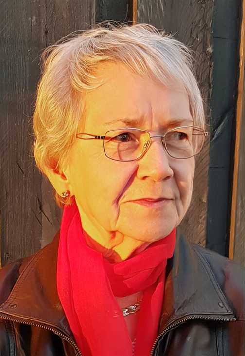 Portr&auml;t einer &auml;lteren Frau mit kurzen, grauen Haaren und Brille, die einen roten Schal und eine schwarze Jacke tr&auml;gt.