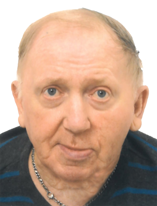 Portr&auml;t eines &auml;lteren Mannes mit kurzen, blonden Haaren und einem grauen Oberteil, mit einem Kettenanh&auml;nger um den Hals.