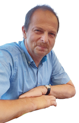 Mann mit Hemd und Armbanduhr, l&auml;chelnd mit verschr&auml;nkten Armen auf einem Tisch. Hintergrund ist einfarbig wei&szlig;.