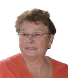 Porträt einer lächelnden älteren Frau mit Brille und kurz geschnittenen Haaren in einem roten Oberteil.