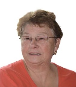 Portr&auml;t einer l&auml;chelnden &auml;lteren Frau mit Brille und kurz geschnittenen Haaren in einem roten Oberteil.