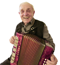 L&auml;chelnder &auml;lterer Mann mit einem roten Akkordeon in der Hand, tr&auml;gt eine schwarze Weste und ein graues Hemd.