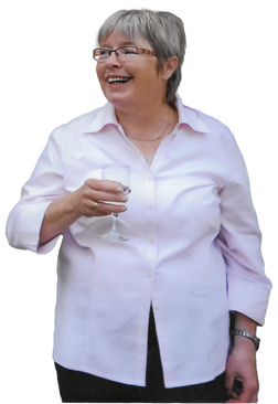 L&auml;chelnde Frau mit kurzem grauen Haar, die ein Glas in der Hand h&auml;lt, tr&auml;gt ein pinkes Hemd und steht frontal.