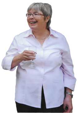 L&auml;chelnde Frau mit kurzem grauen Haar, die ein Glas in der Hand h&auml;lt, tr&auml;gt ein pinkes Hemd und steht frontal.