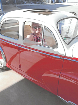 Frau mit Sonnenbrille sitzt in einem roten Oldtimer, Fenster offen, im Freien auf einer sonnigen Stra&szlig;e.