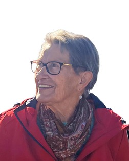 Lächelnde ältere Frau mit Brille, roter Jacke und Halstuch, blickt nach oben vor hellem Hintergrund.