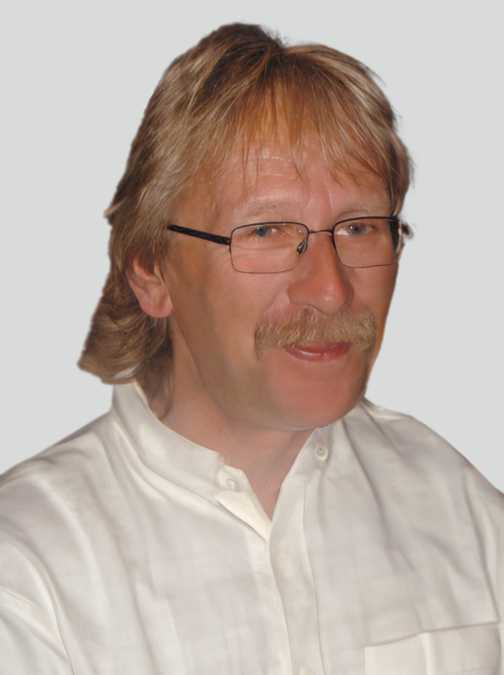 Portr&auml;t eines l&auml;chelnden Mannes mit Brille und blonden, leicht gewellten Haaren, in einem wei&szlig;en Hemd.