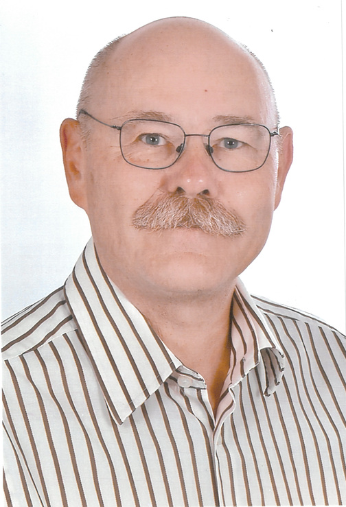 Portr&auml;t eines Mannes mit Brille und Schnurrbart, gekleidet in ein gestreiftes Hemd mit hellen und dunklen Linien.