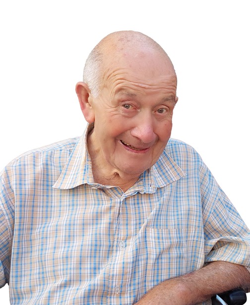 L&auml;chelnder &auml;lterer Mann mit Glatze, tr&auml;gt ein kariertes Hemd, sitzt auf einem Rollstuhl vor wei&szlig;em Hintergrund.