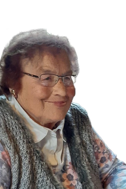 Portrait einer &auml;lteren Frau mit Brille, l&auml;chelnd, in einem grauen Strickpulli &uuml;ber blumigem Oberteil.