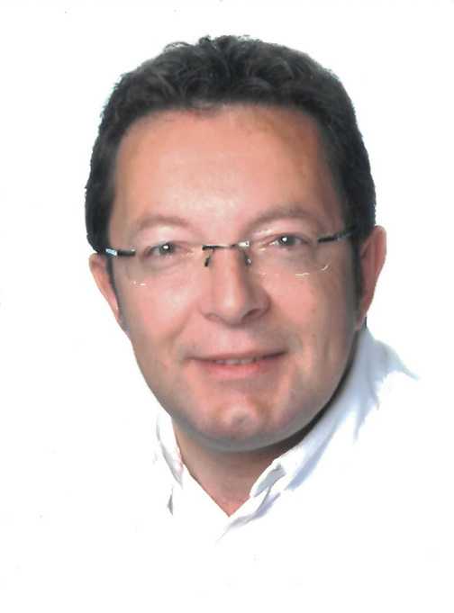 Portr&auml;t eines Mannes mit Brille, der l&auml;chelt, vor einem wei&szlig;en Hintergrund. Er tr&auml;gt ein helles Oberteil.