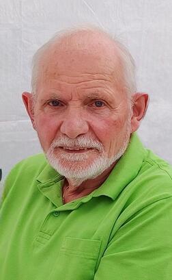 Portr&auml;t eines &auml;lteren Mannes mit grauem Bart, der ein gr&uuml;nes Polohemd tr&auml;gt, vor einem wei&szlig;en Hintergrund.