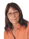 Portr&auml;t einer Frau mit langen braunen Haaren, die eine orange Bluse und eine Goldkette tr&auml;gt. Hintergrund ist wei&szlig;.