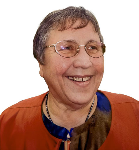 L&auml;chelnde Frau mit Brille und kurzem Haar, tr&auml;gt einen orangefarbenen Blazer und sitzt vor einem wei&szlig;en Hintergrund.