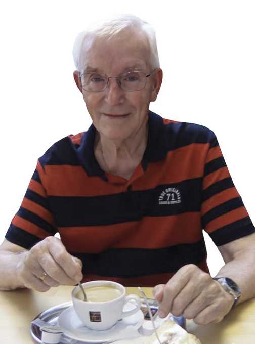 &Auml;lterer Mann mit Brille, der in einer Tasse Kaffee r&uuml;hrt, sitzt an einem Tisch mit einer Kuchenteller.