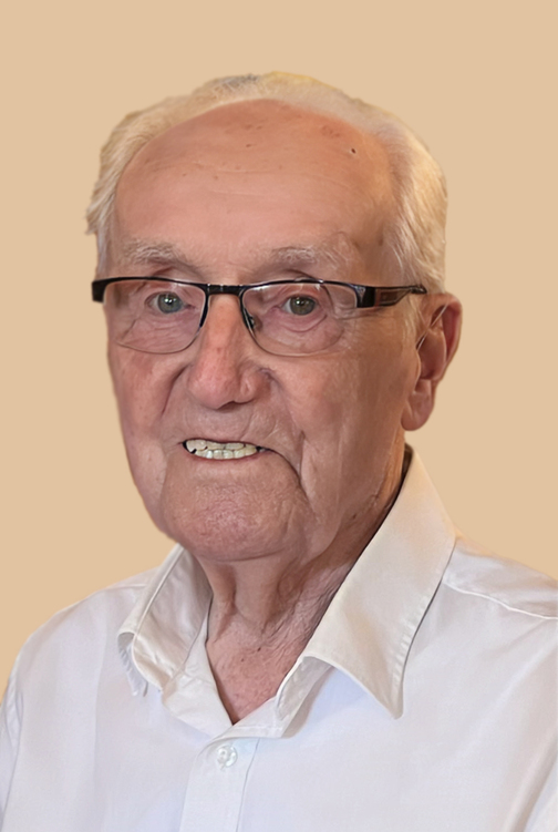 Portr&auml;t eines &auml;lteren Mannes mit Brille, l&auml;chelnd, in einem wei&szlig;en Hemd vor einem beigen Hintergrund.