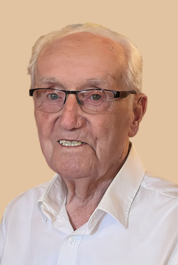 Portr&auml;t eines &auml;lteren Mannes mit Brille, l&auml;chelnd, in einem wei&szlig;en Hemd vor einem beigen Hintergrund.