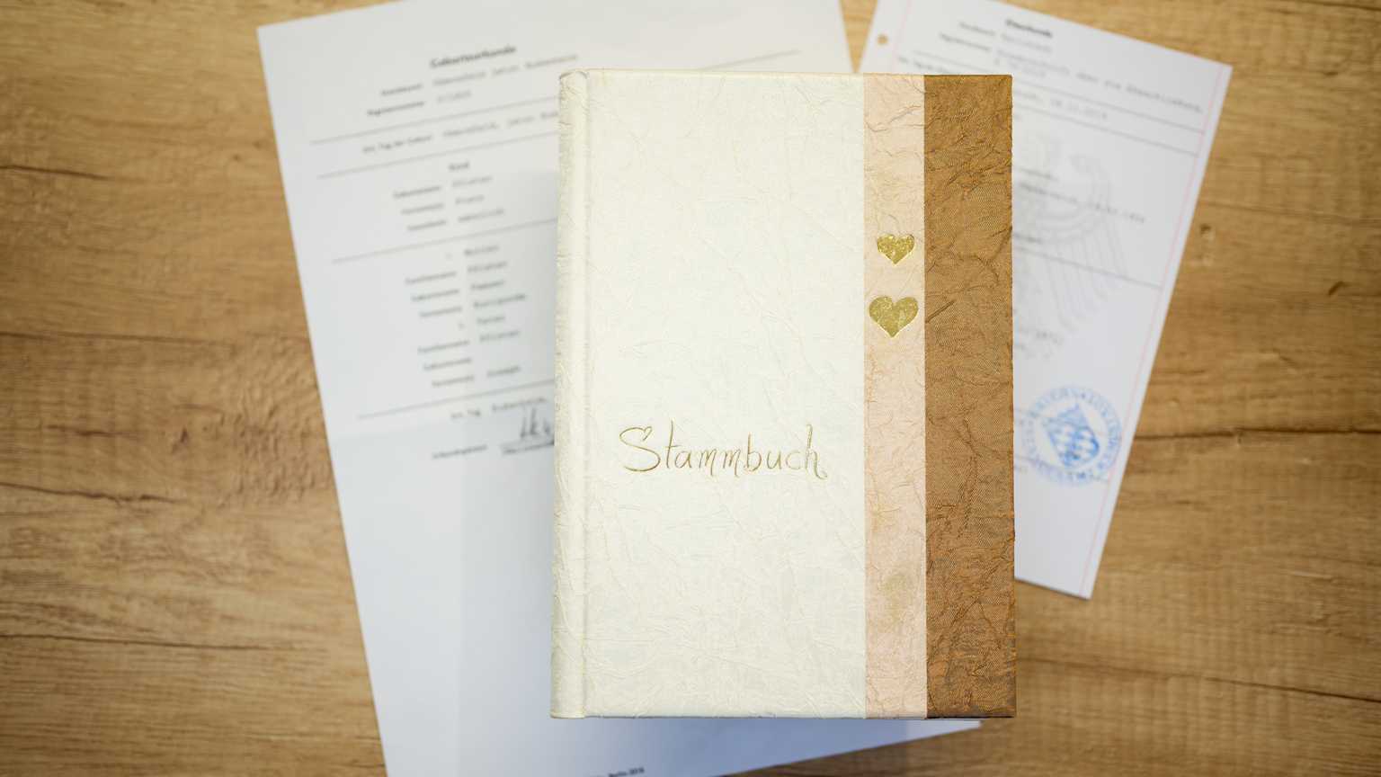 Stammbaum-Buch auf einem Holztisch, umgeben von offiziellen Dokumenten zur Geburt.