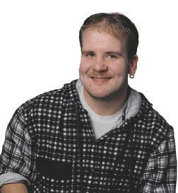 Portrait eines l&auml;chelnden Mannes mit kurzen Haaren, einem karierten Hemd und einem Ohringe. Hintergrund ist wei&szlig;.