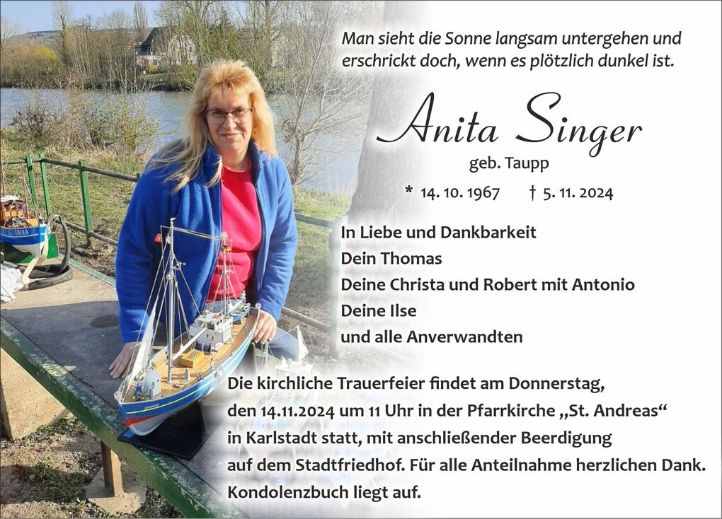 Frau mit langen blonden Haaren sitzt neben einem Modellschiff auf einer Bank am Wasser, umgeben von Natur.