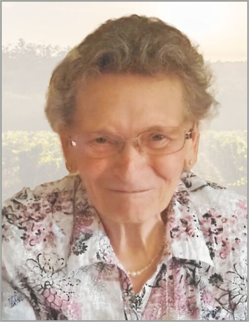 &Auml;ltere Frau mit Brille und blumigem Hemd l&auml;chelt vor unscharfem Hintergrund von Weinbergen.