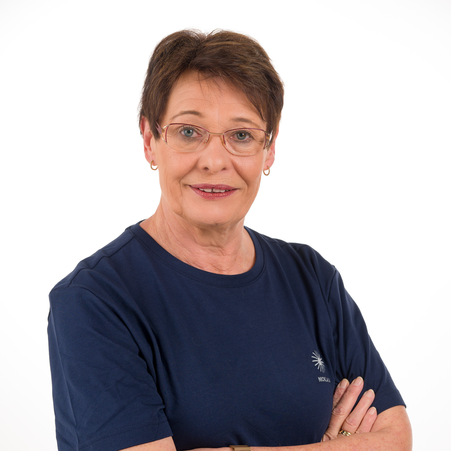 Portr&auml;t einer l&auml;chelnden Frau mit kurzen Haaren, Brille und blauer T-Shirt, die die Arme vor der Brust verschr&auml;nkt.