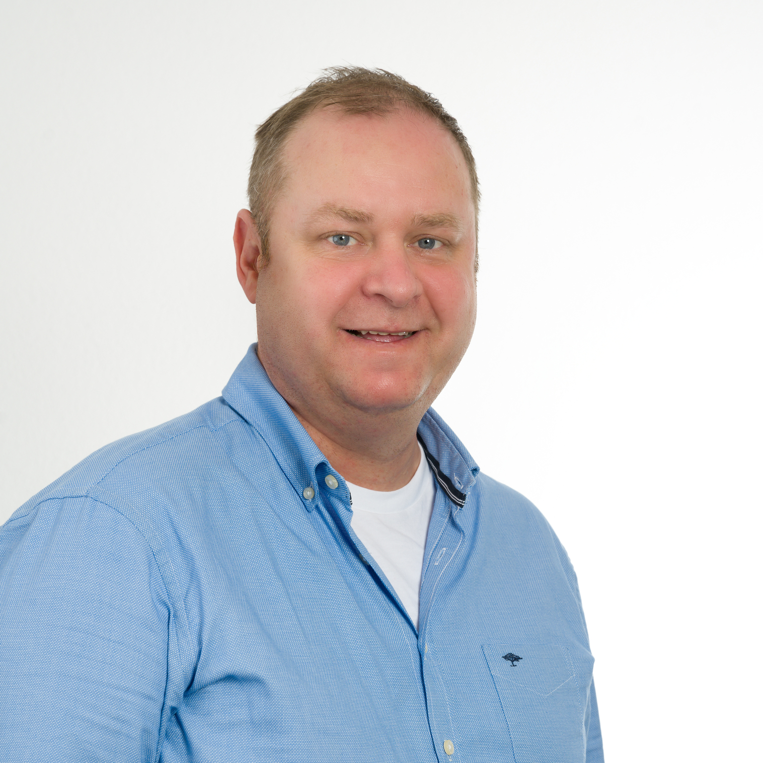 Portr&auml;t eines Mannes mit kurzen Haaren in einem blauen Hemd vor einem hellen Hintergrund. Er l&auml;chelt freundlich in die Kamera.