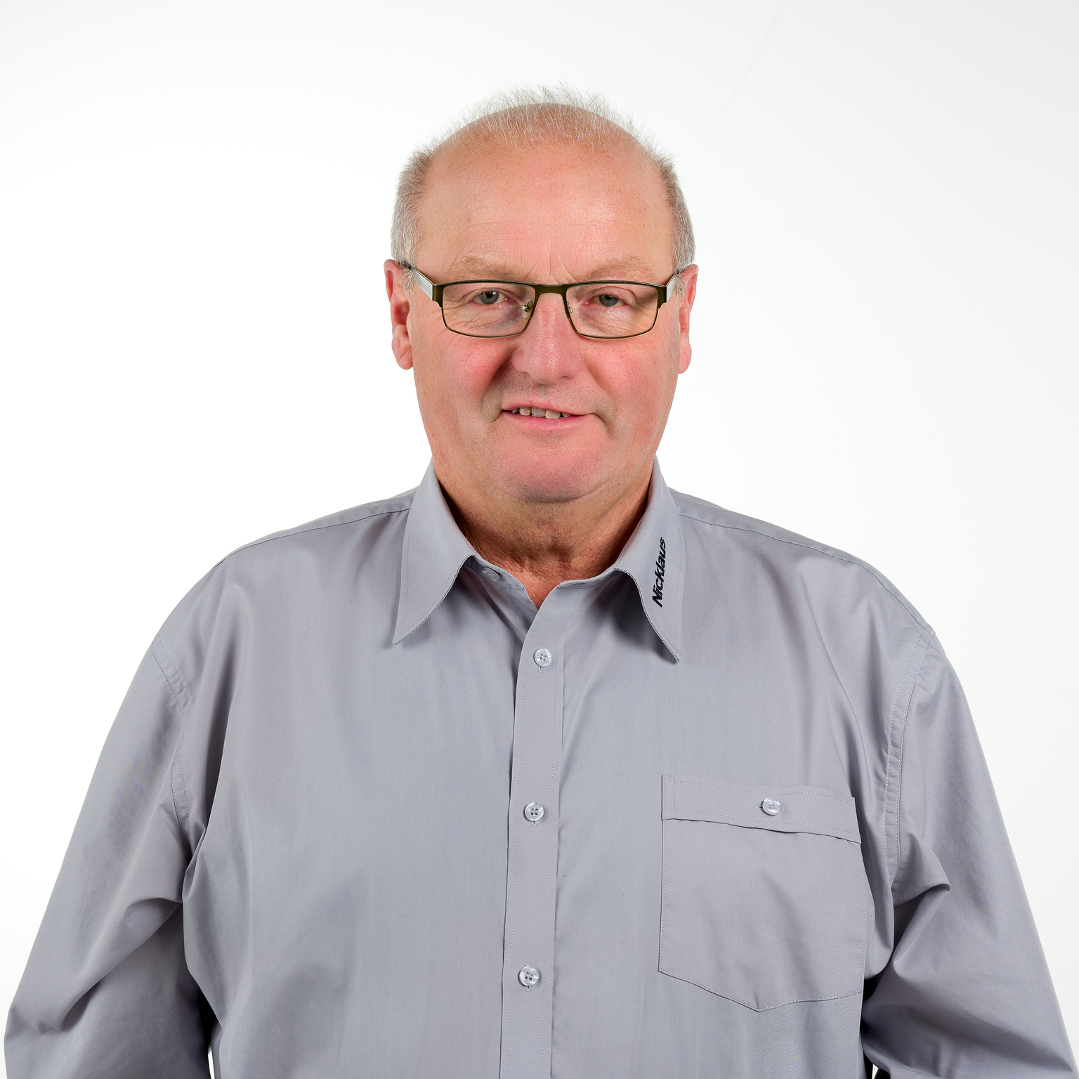 Portr&auml;t eines Mannes mit Brille, grauhem Hemd und kurzen Haaren, vor einem wei&szlig;en Hintergrund.