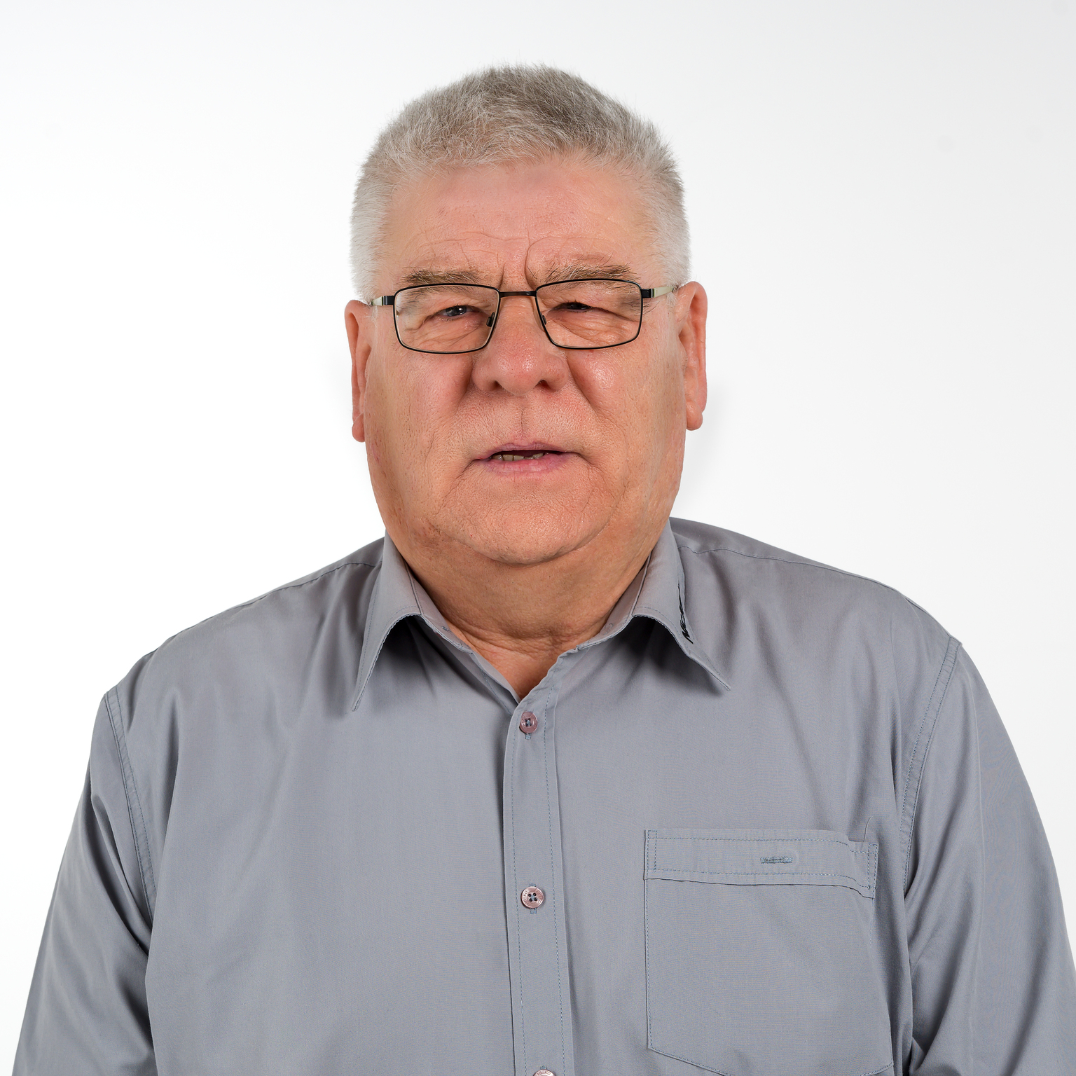 Portr&auml;t eines &auml;lteren Mannes mit Brille, in einem grauen Hemd vor einem wei&szlig;en Hintergrund.