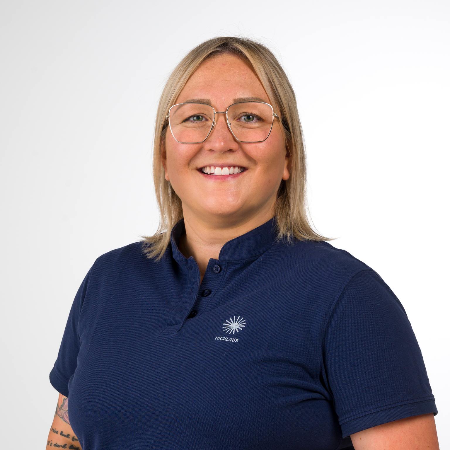 Portrait einer l&auml;chelnden Frau mit kurzen blonden Haaren, Brille und dunkelblauem Polohemd. Hintergrund ist hell.