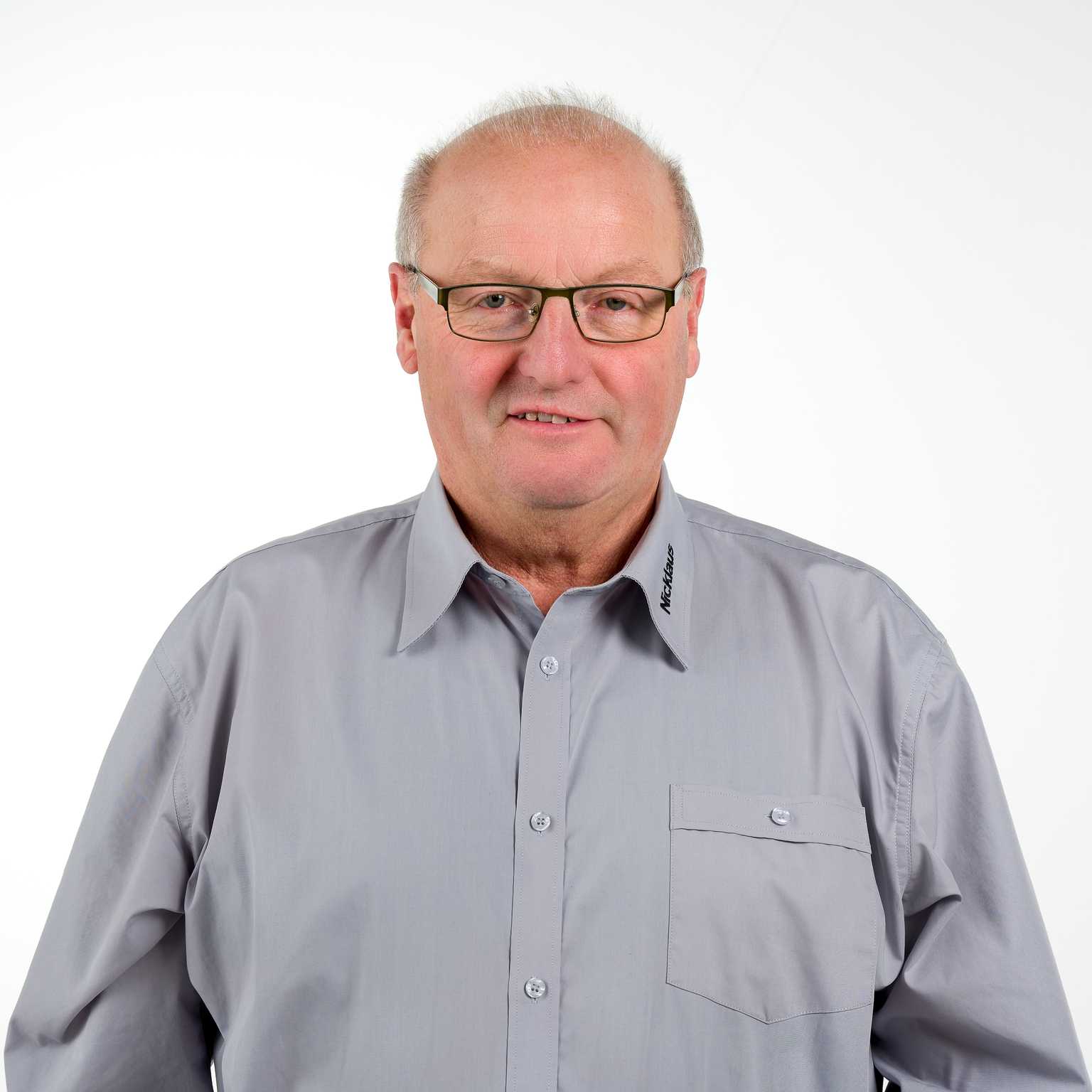 Portr&auml;t eines Mannes mit Brille, grauhem Hemd und kurzen Haaren, vor einem wei&szlig;en Hintergrund.